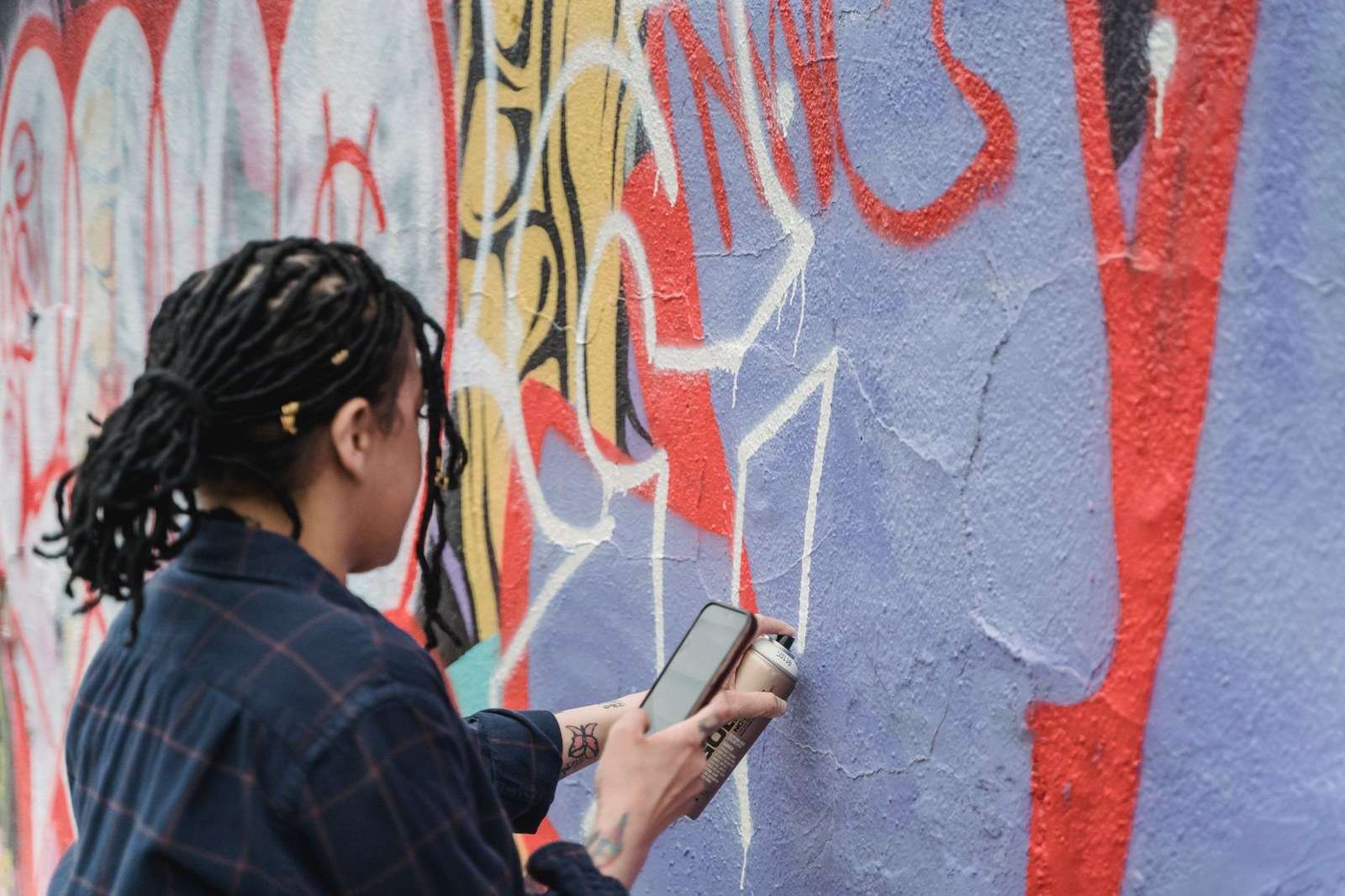 An artist painting a large colorful mural on an exterior city wall