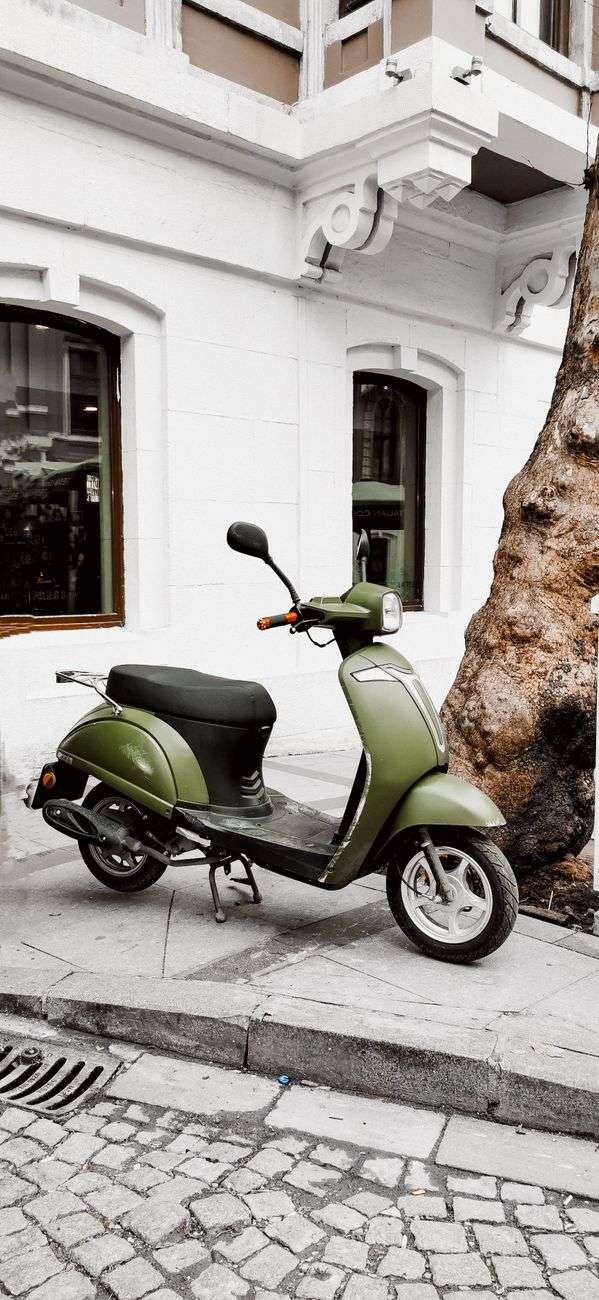A green moped-style scooter parked on a cobblestone street beside a building