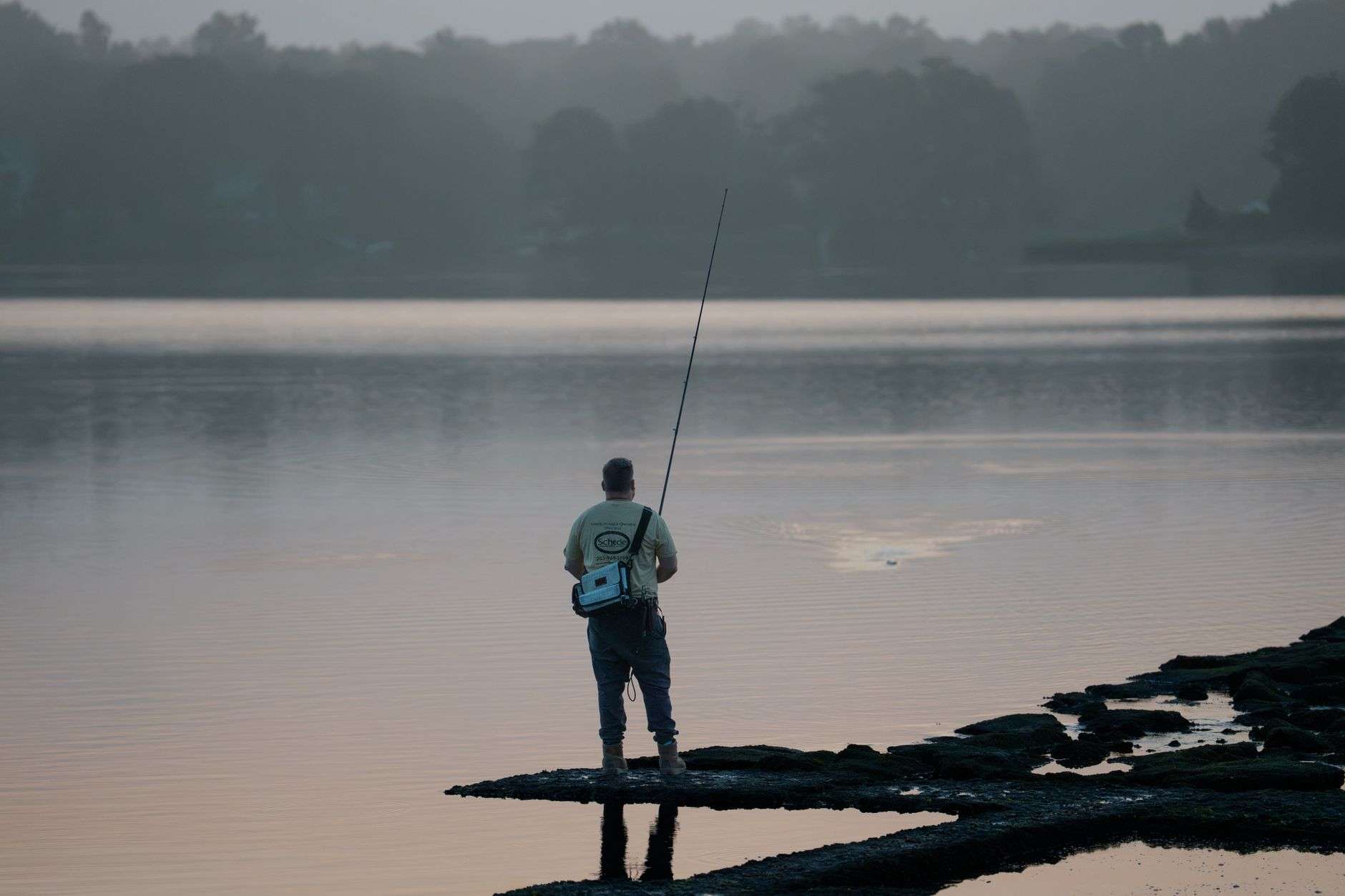 Person fishing from the shore of a calm lake at sunrise