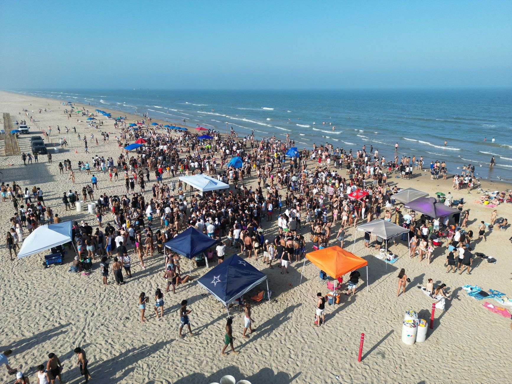 Crowds walking among vendor tents at an outdoor beach festival beside the Gulf of Mexico