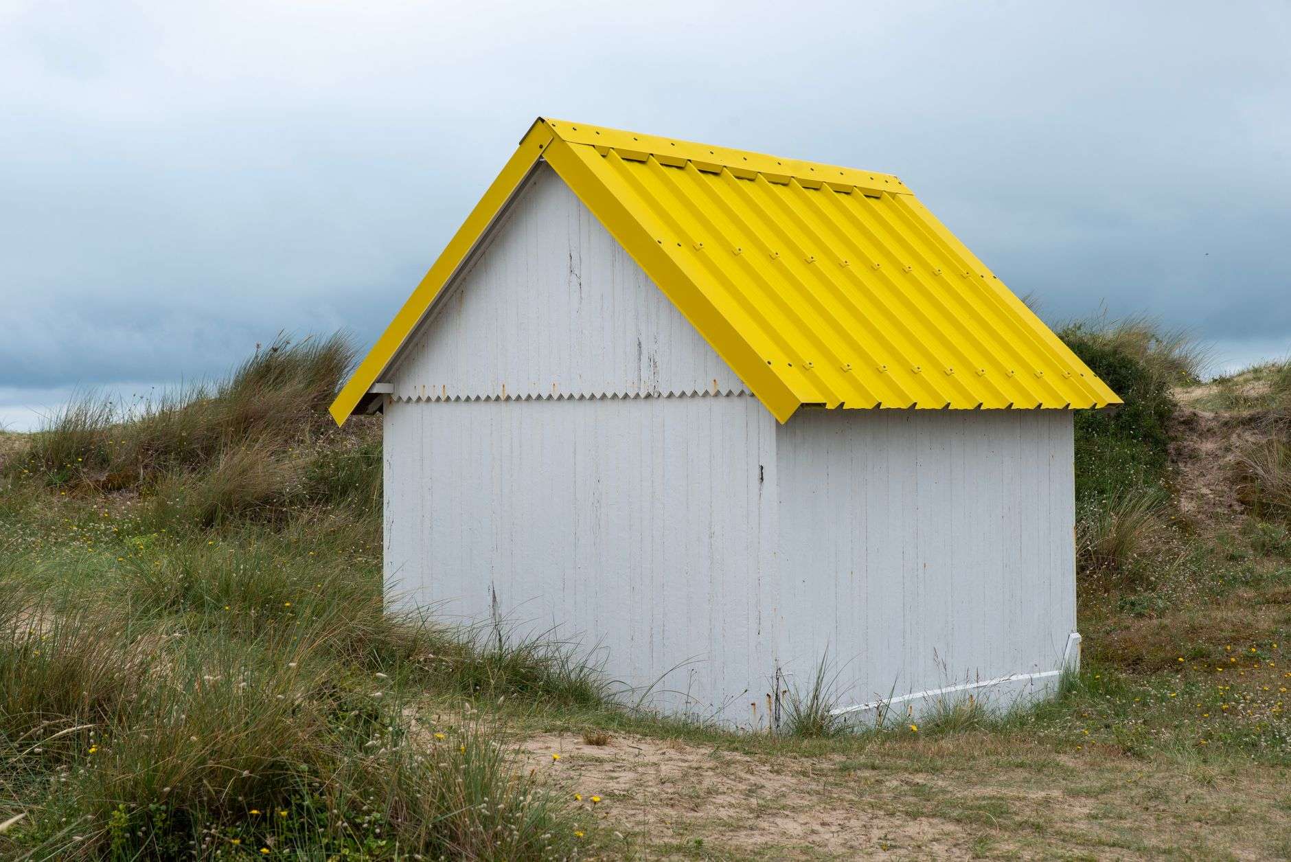 A yellow wood-frame beach cottage with a porch near the coast