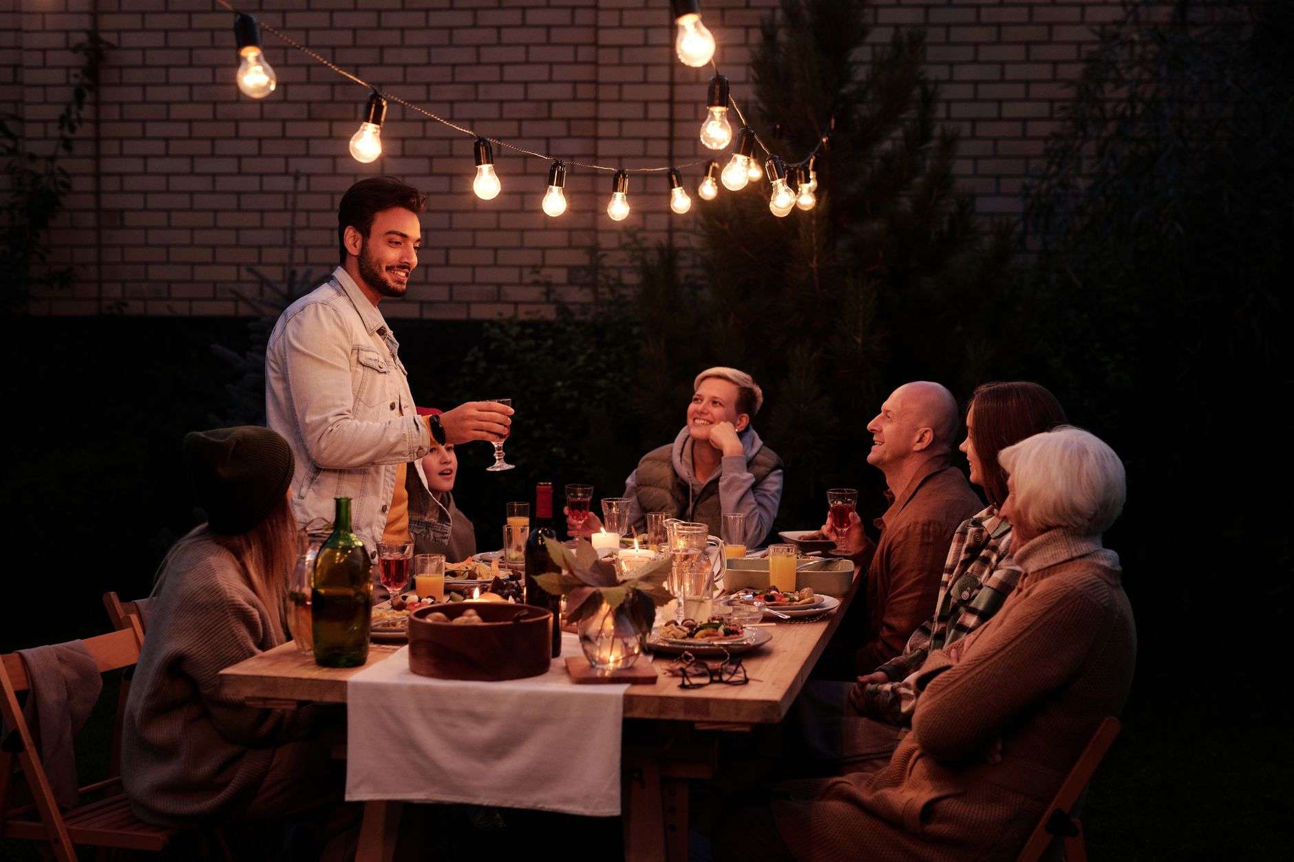 A long dinner table set outdoors under string lights, illustrating a street-set multi-course dinner event