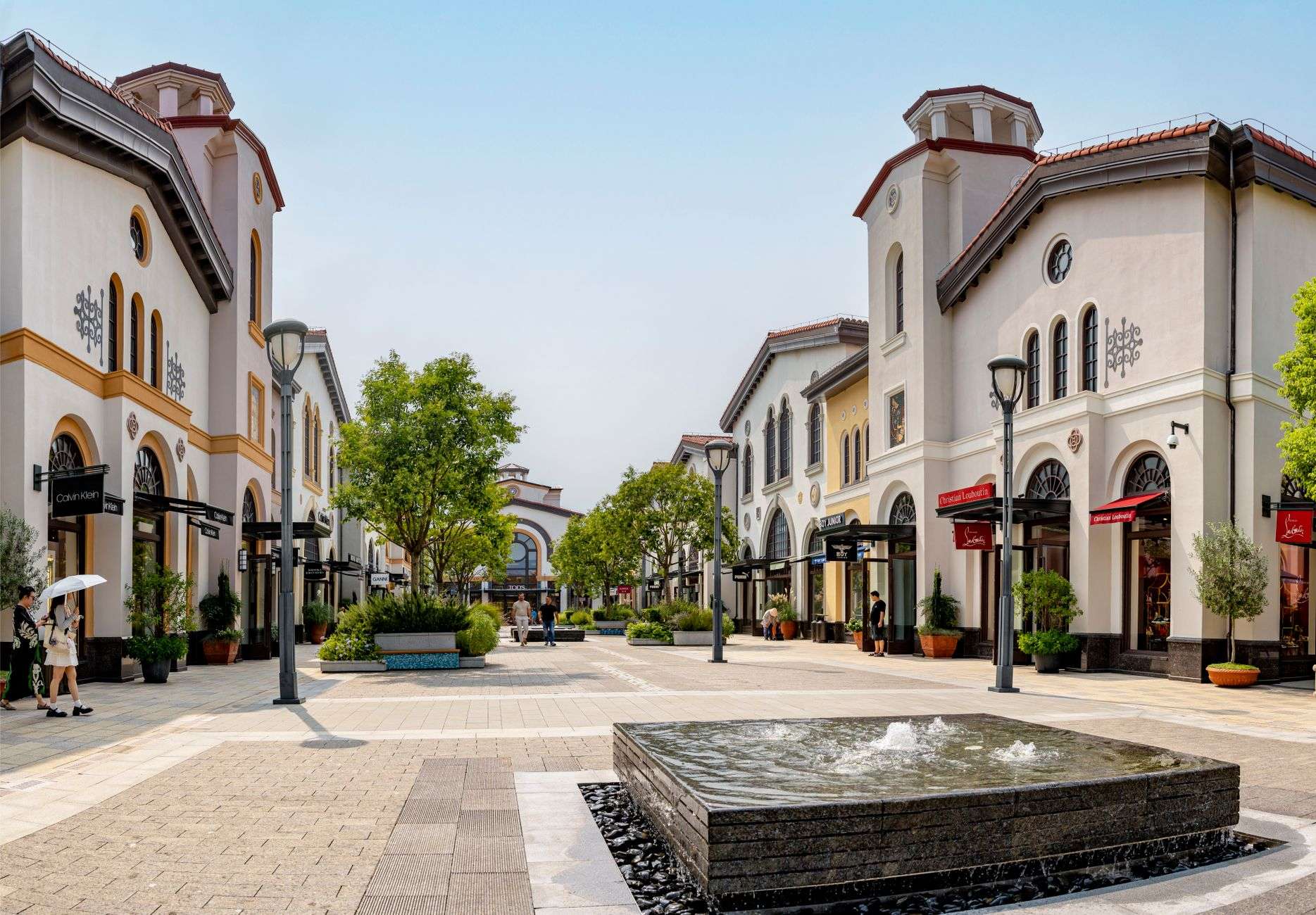 Shoppers walking past storefronts along an open-air outlet shopping center walkway