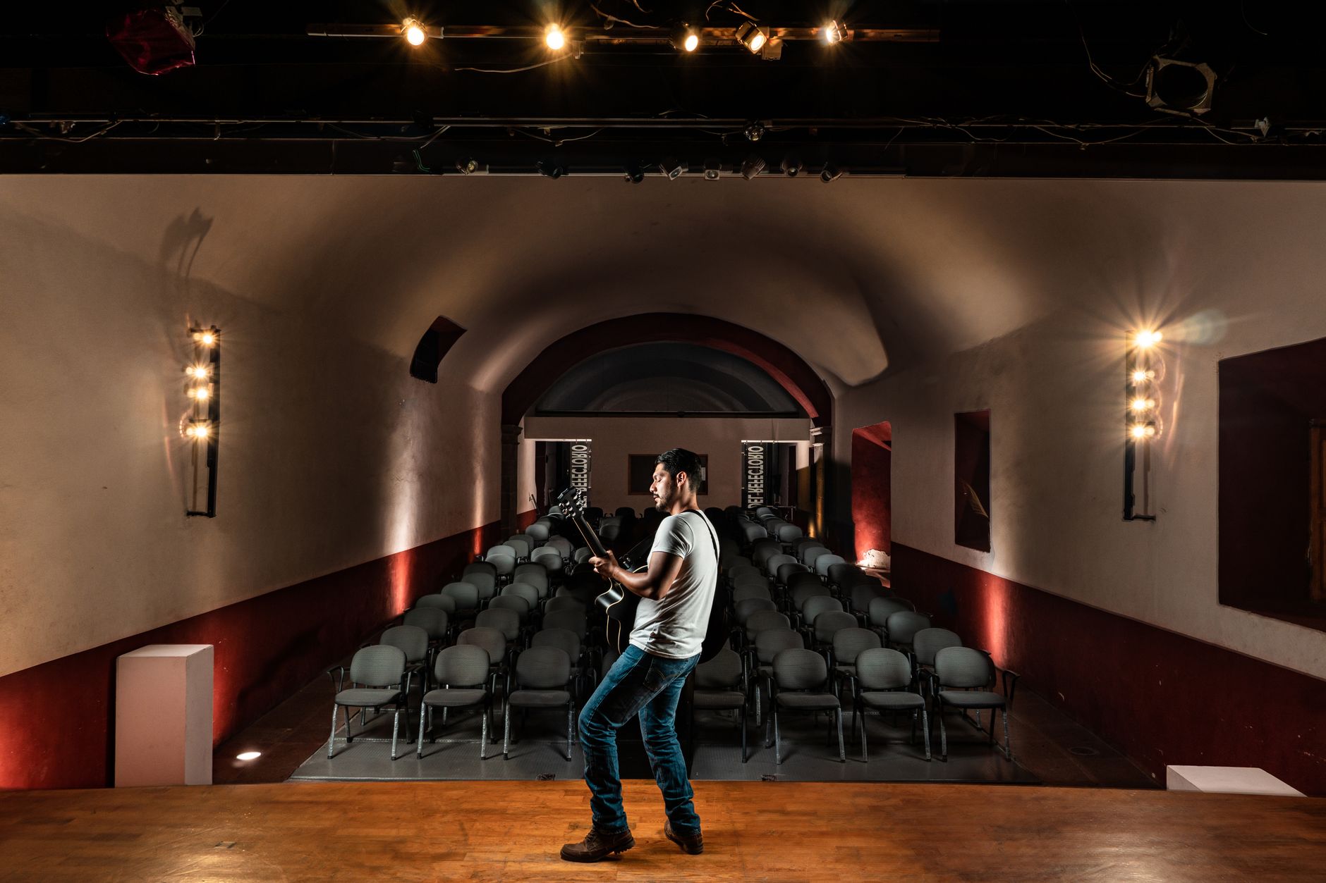 Performer on a small theater stage under warm concert lights with seated audience