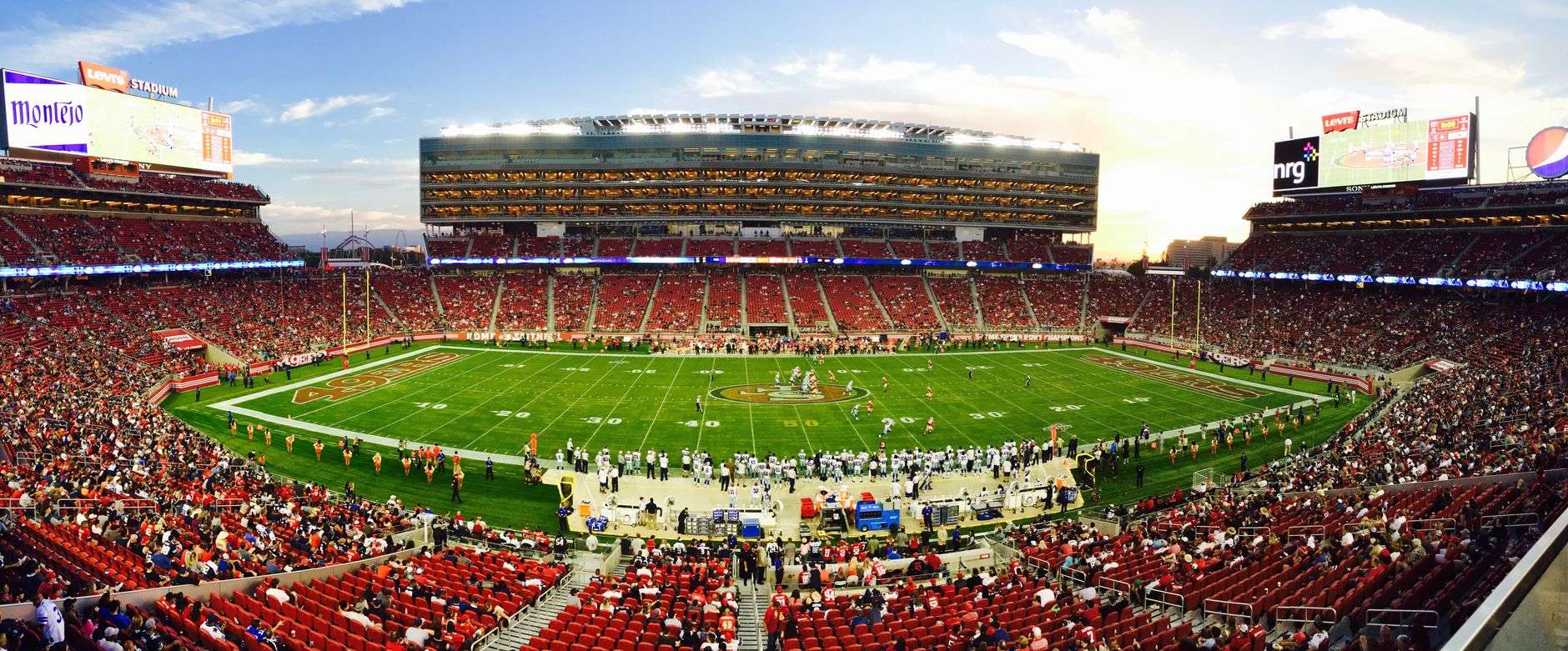 A packed football stadium under the lights during a night game