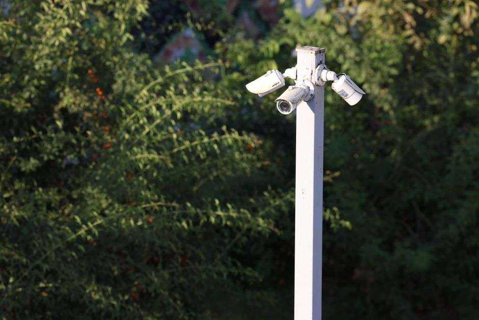 A surveillance camera mounted high on a pole above a street