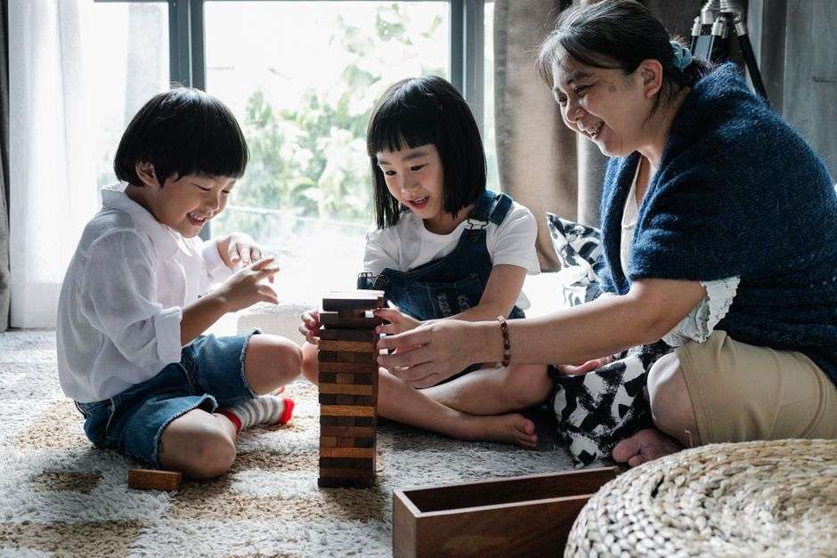 A grandmother playing and laughing with young children outdoors in a backyard