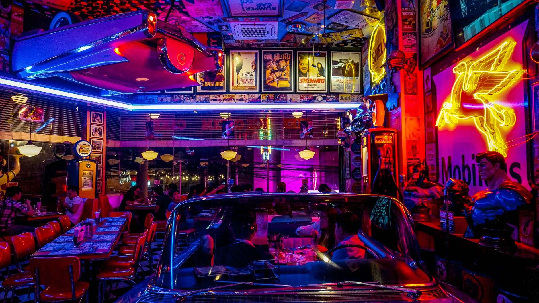 Neon-lit retro diner interior with red booths, a vintage car and framed movie posters