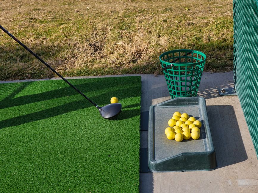 A golfer swinging a club on a practice range with rows of balls