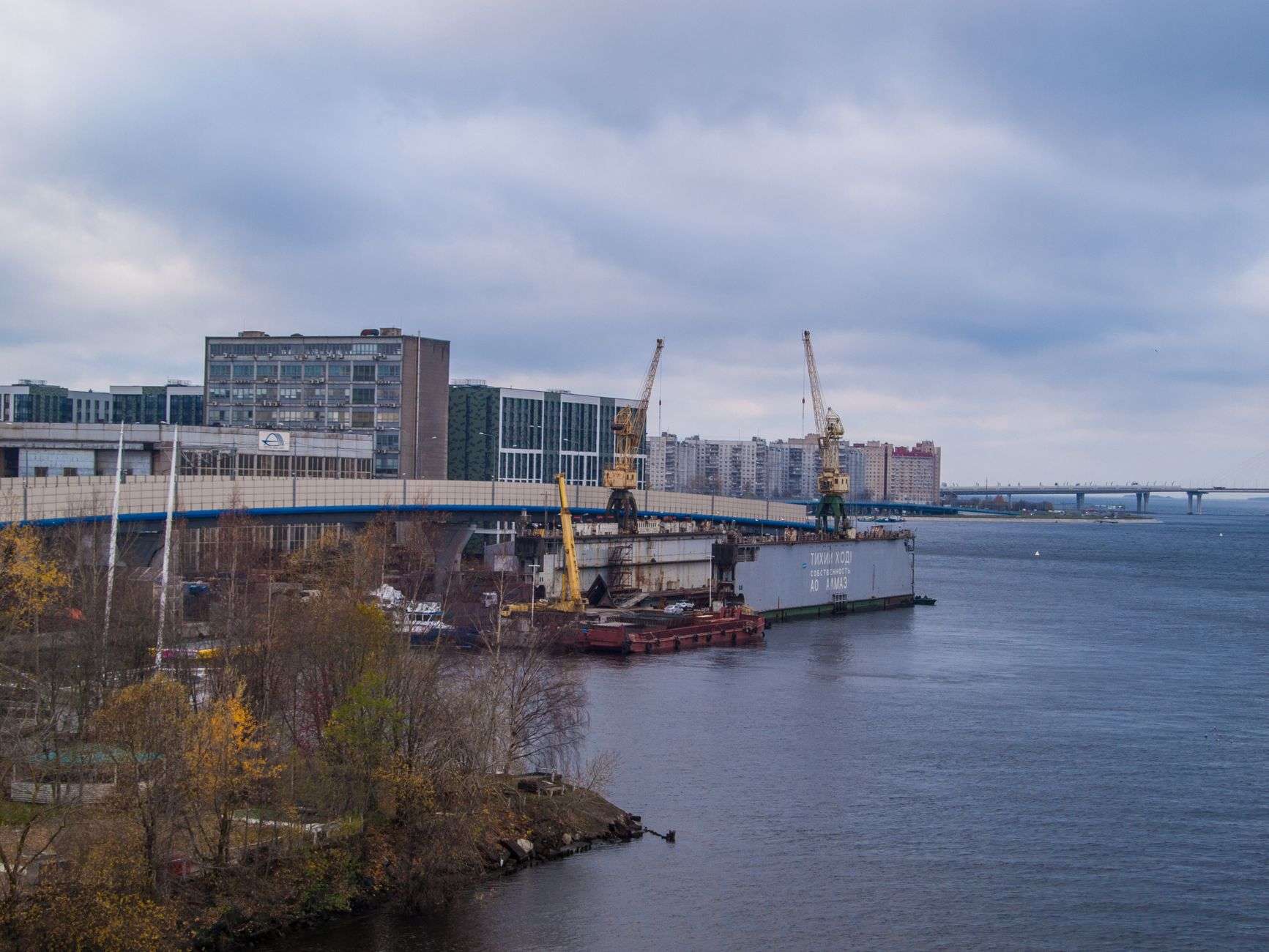 Construction cranes and a bridge under construction along a river under cloudy skies