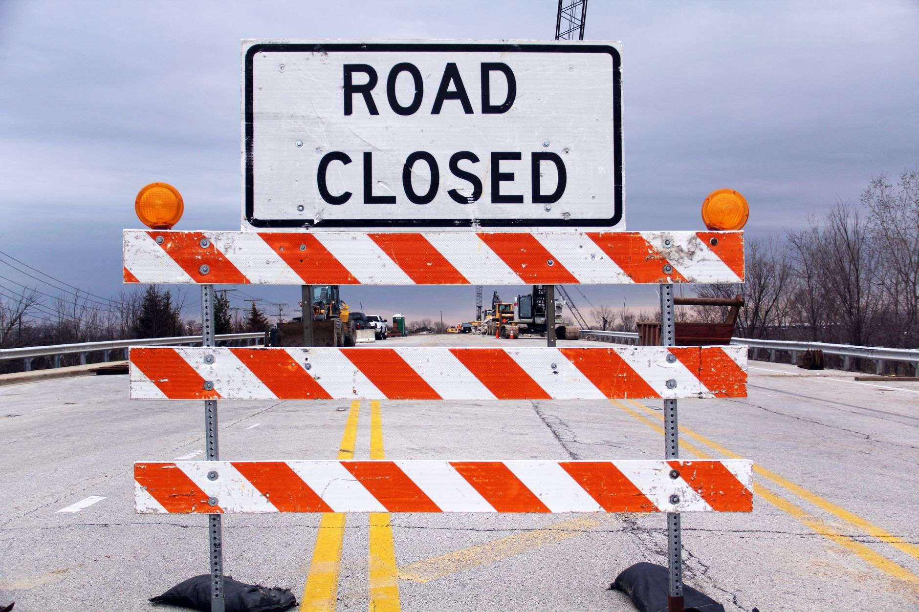 A Road Closed sign mounted on red and white striped barricades across a road