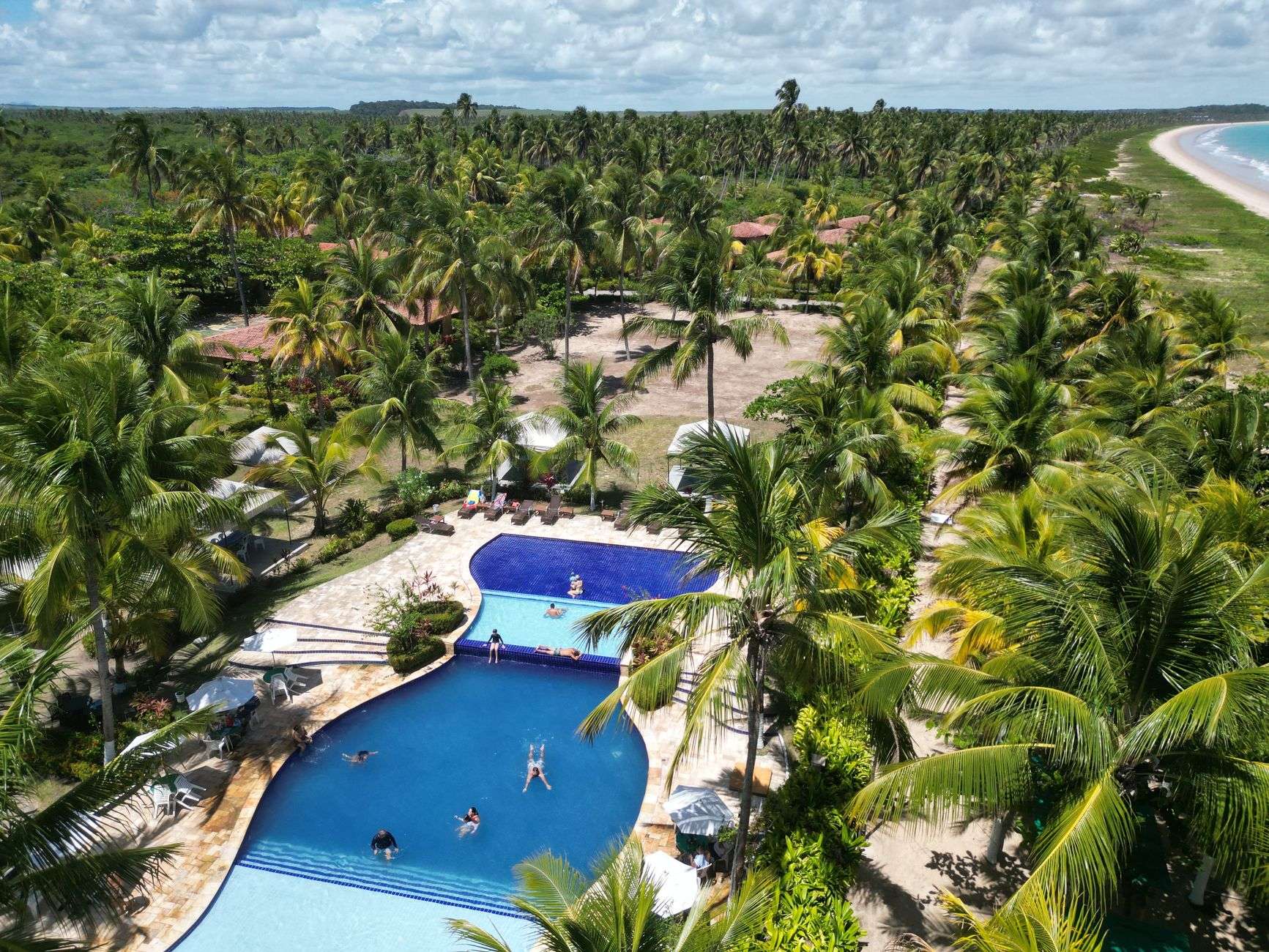Resort pool deck with lounge chairs overlooking a sandy beach and the ocean