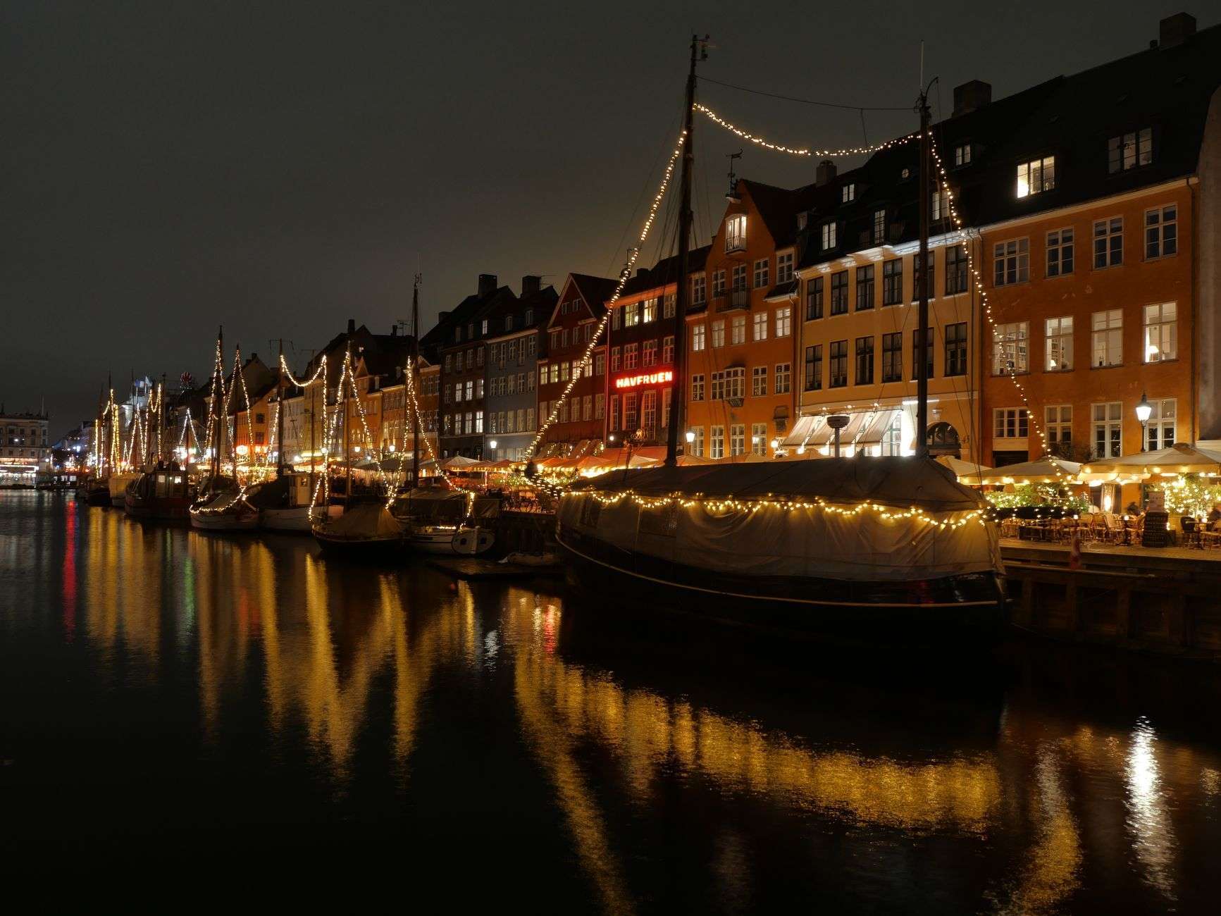 A boat decorated with colorful holiday lights cruising on calm water at night