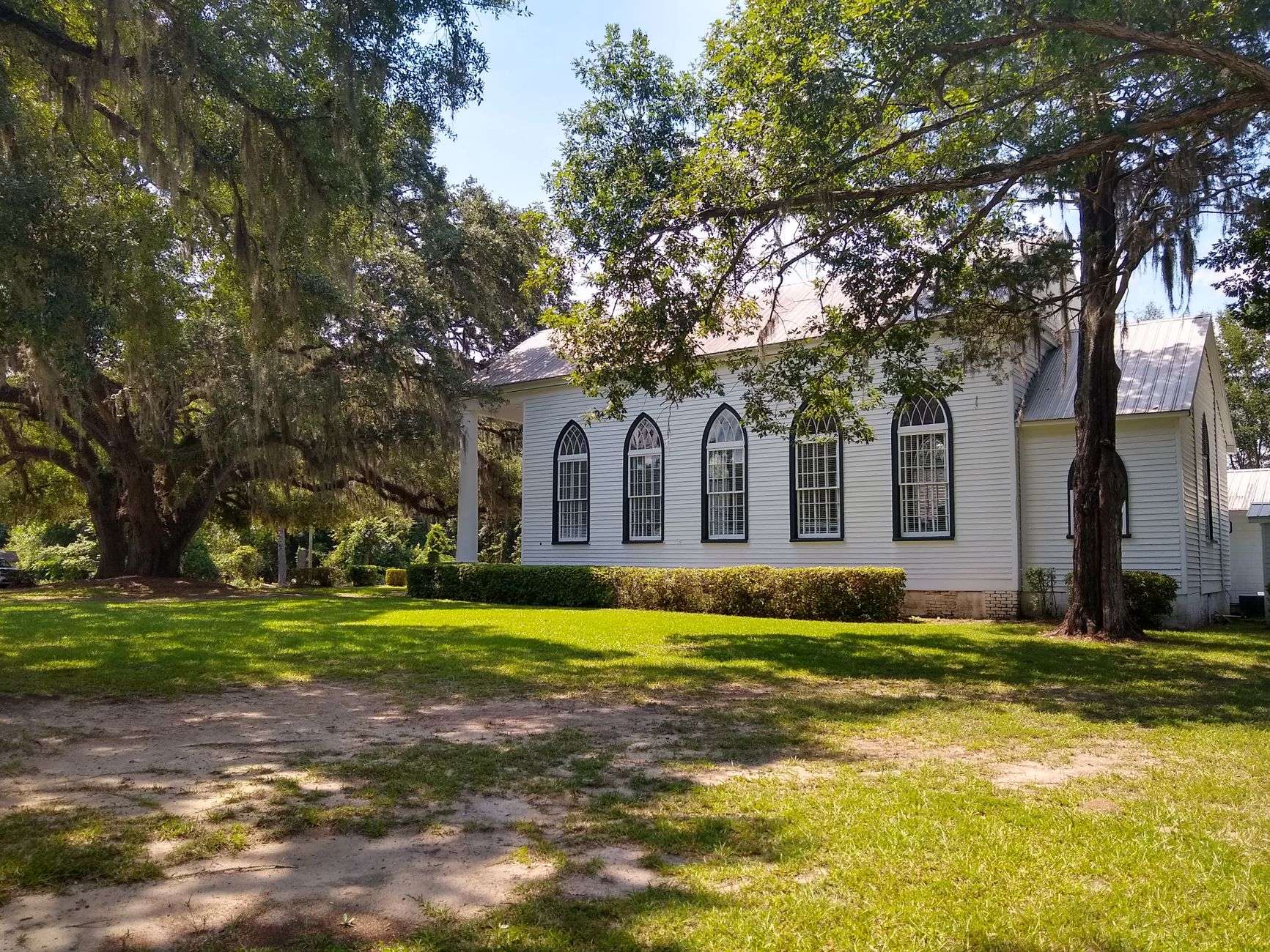 An older wooden church framed by large oak trees