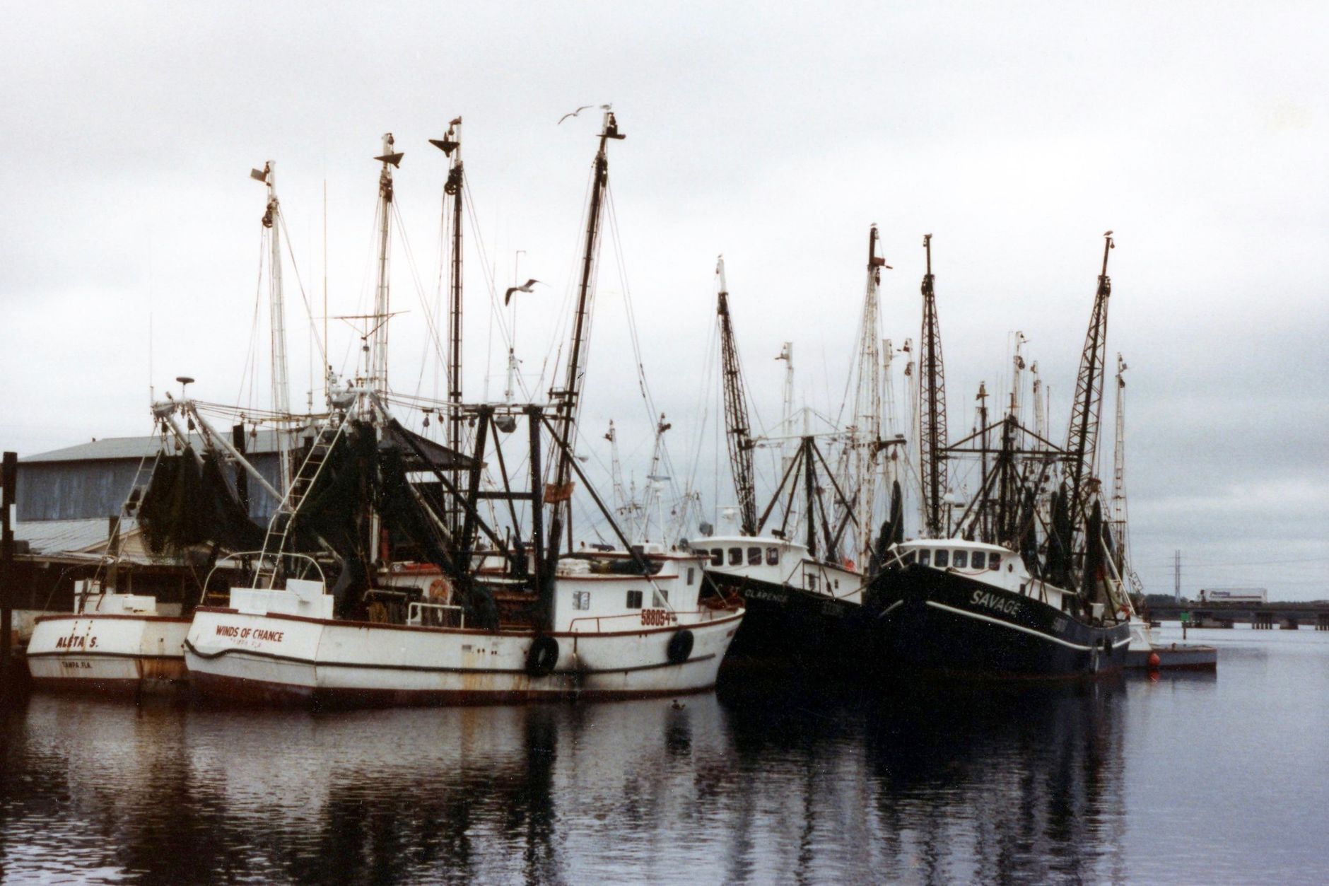 A shrimp trawler with nets raised tied up at a marina dock