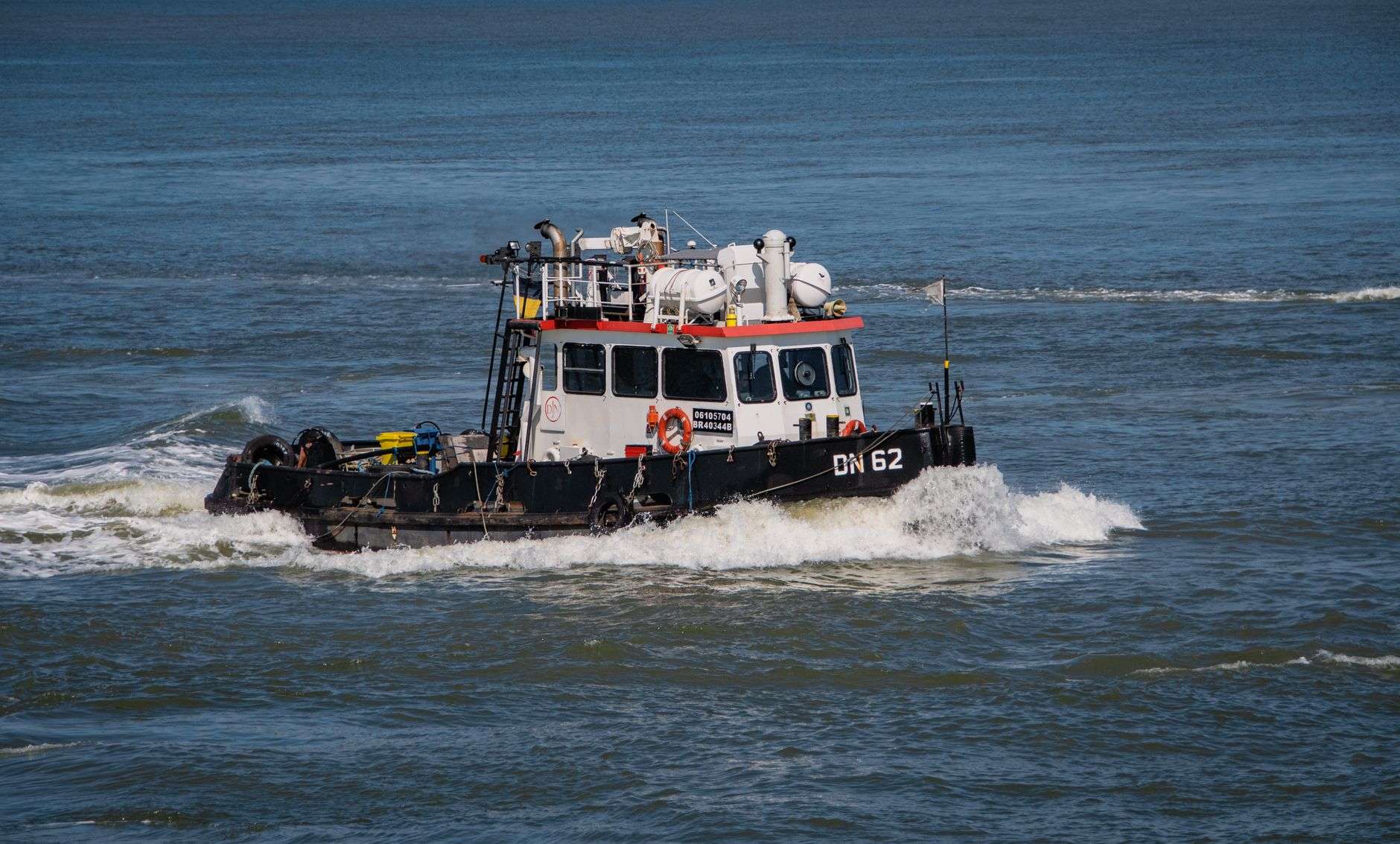 Small black-and-white workboat plowing through choppy, whitecapped water
