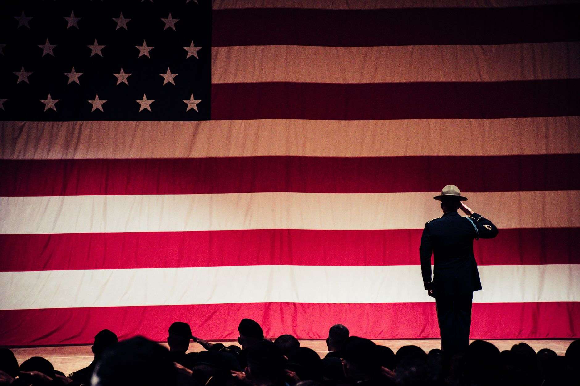 A uniformed soldier saluting before a large American flag