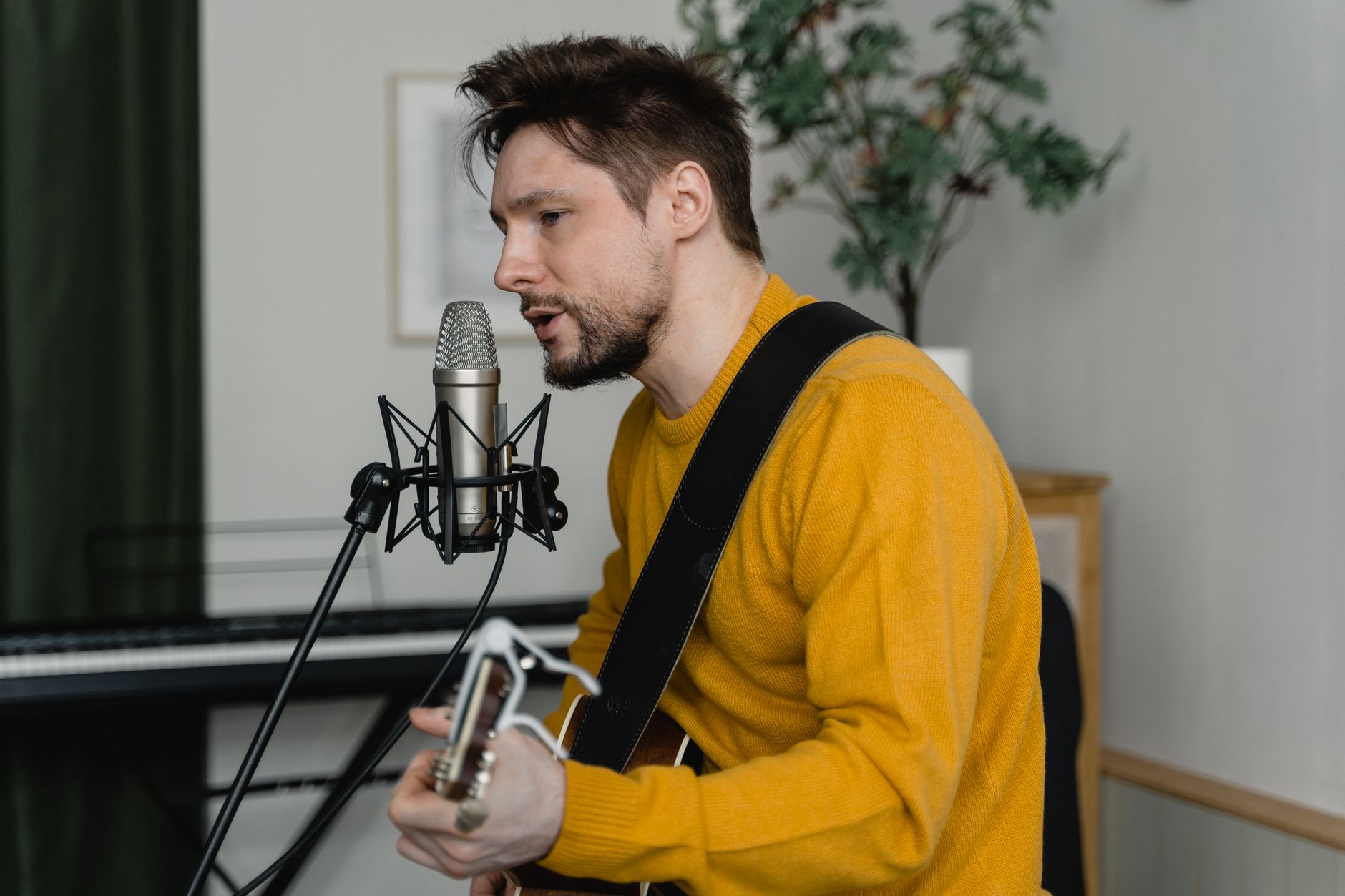 A musician plays an acoustic guitar and sings into a microphone on a small stage