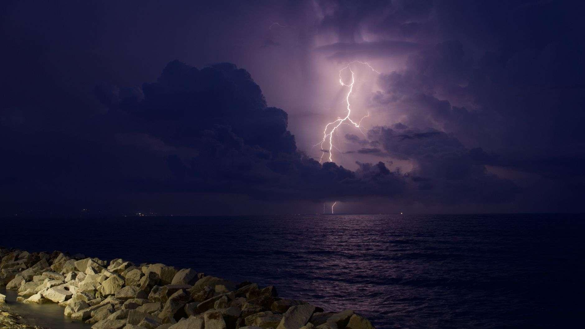 Tall thunderstorm clouds building over a coastal landscape in late afternoon light