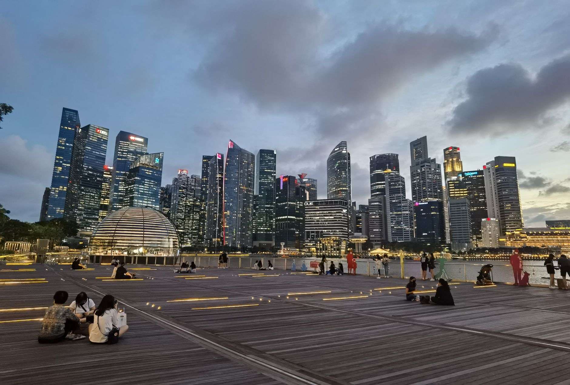 A waterfront marina and boardwalk entertainment district lit at dusk