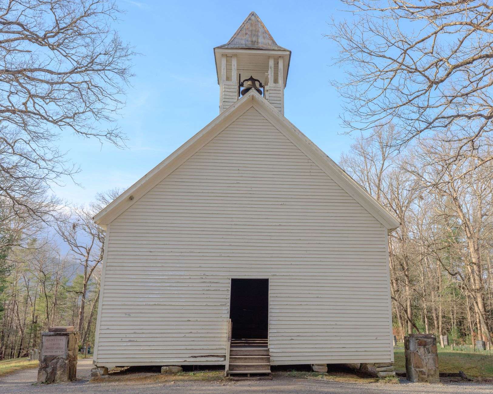 A small white wooden chapel with a peaked roof under trees