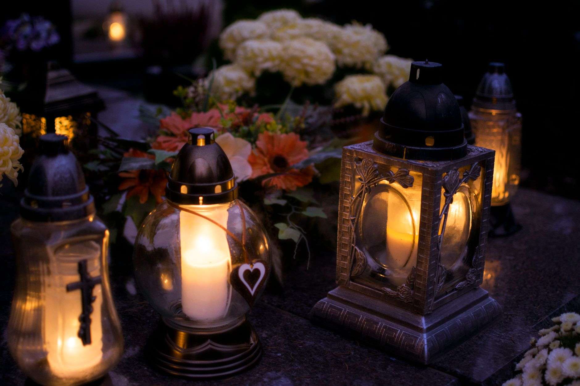 A lit memorial candle placed beside white flowers