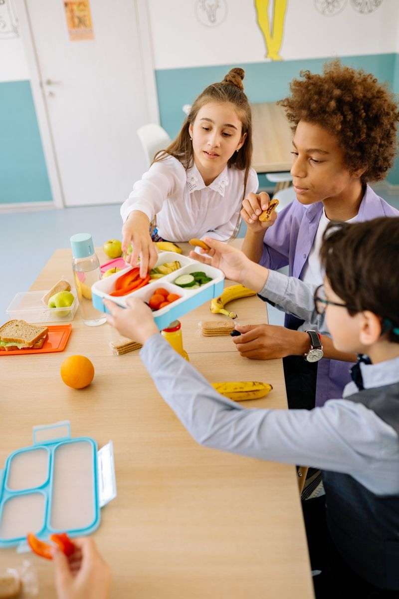 Schoolchildren sharing fruit, sandwiches and packed lunches at a classroom table