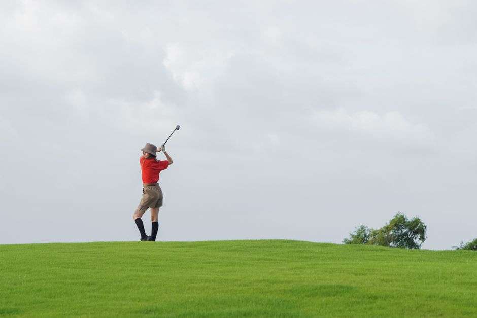 An older woman swinging a golf club on a golf course fairway