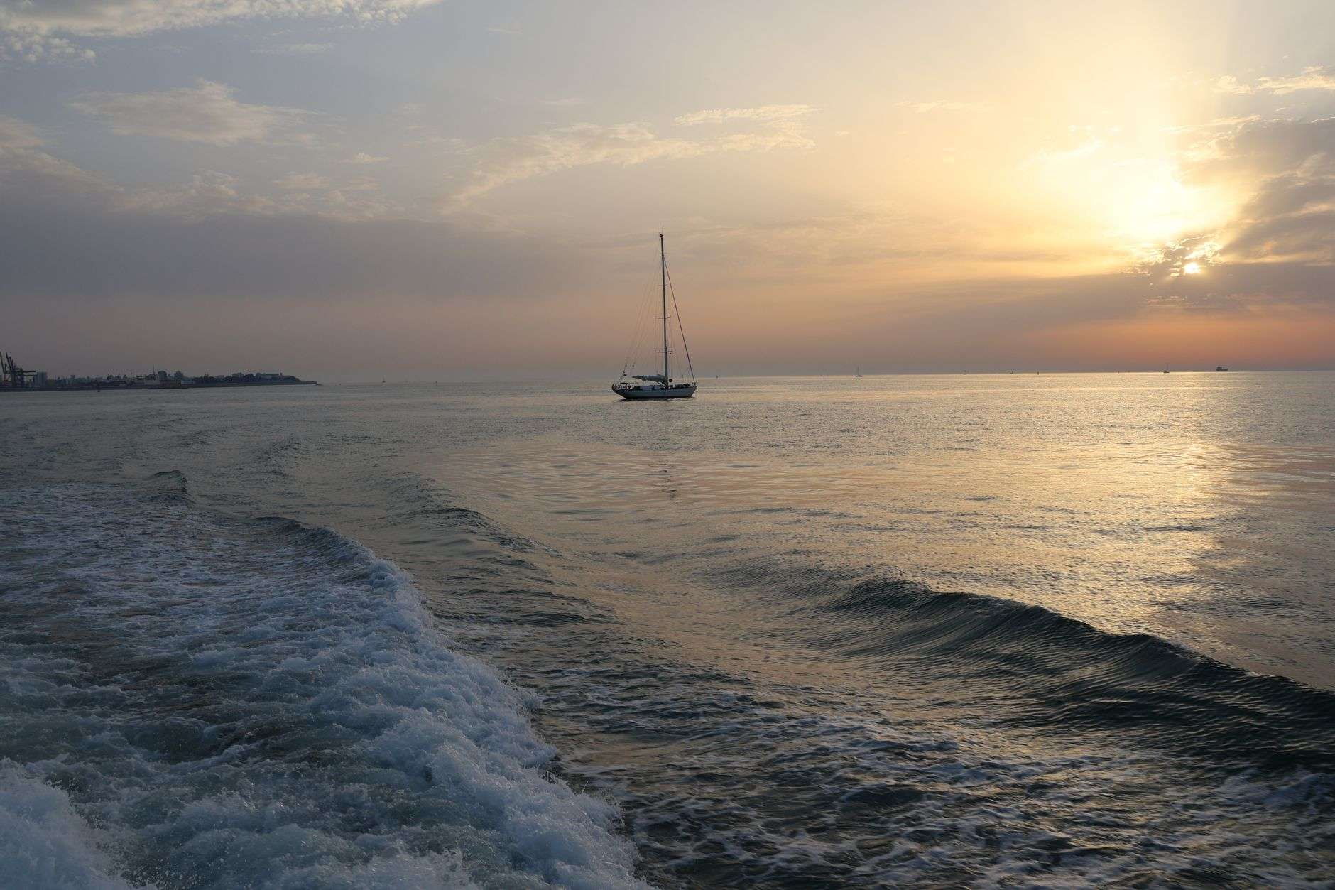 Sailboat gliding across calm water under a colorful sunset sky