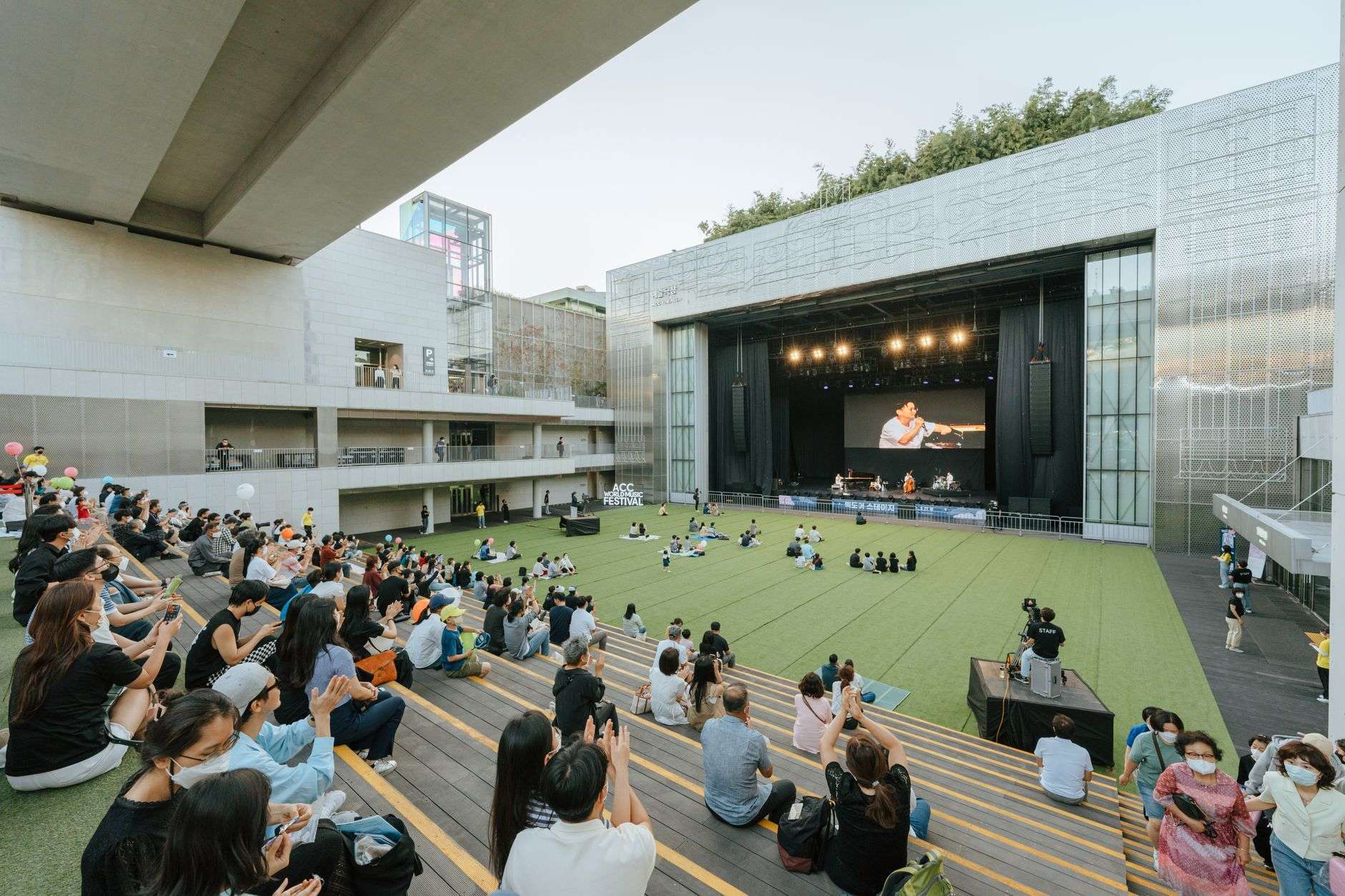 Concertgoers relaxing on a grassy lawn during an outdoor evening concert