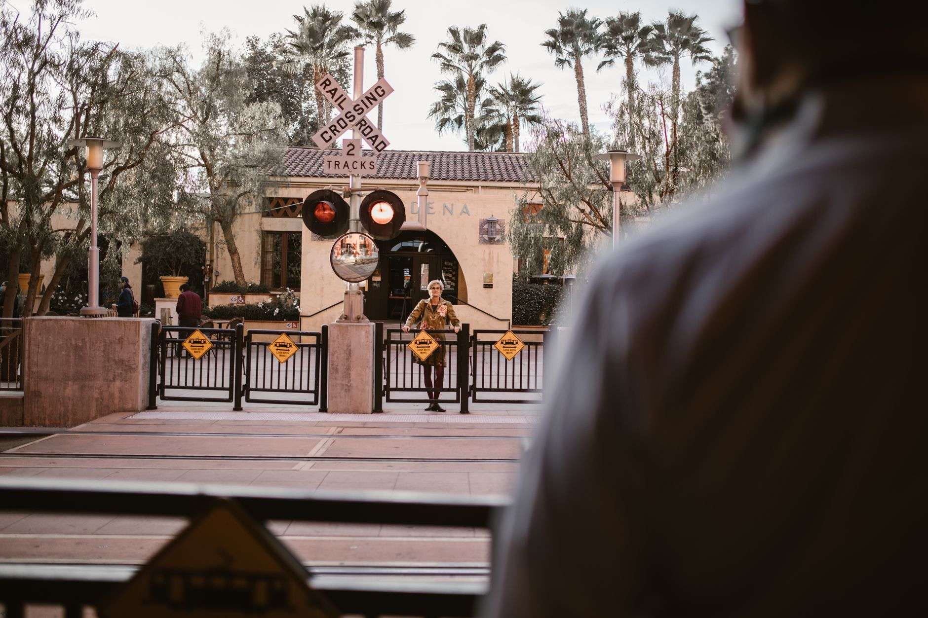 Person waiting at a railroad crossing with safety gates and signs