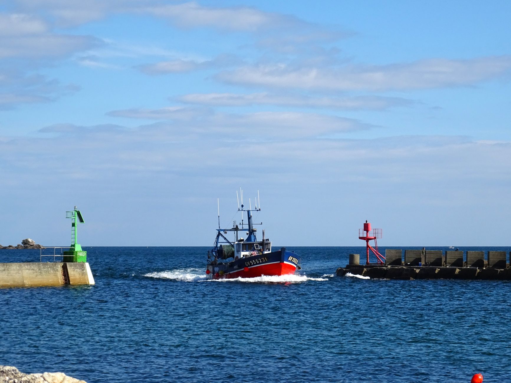 A small fishing boat on calm bay water near a channel marker