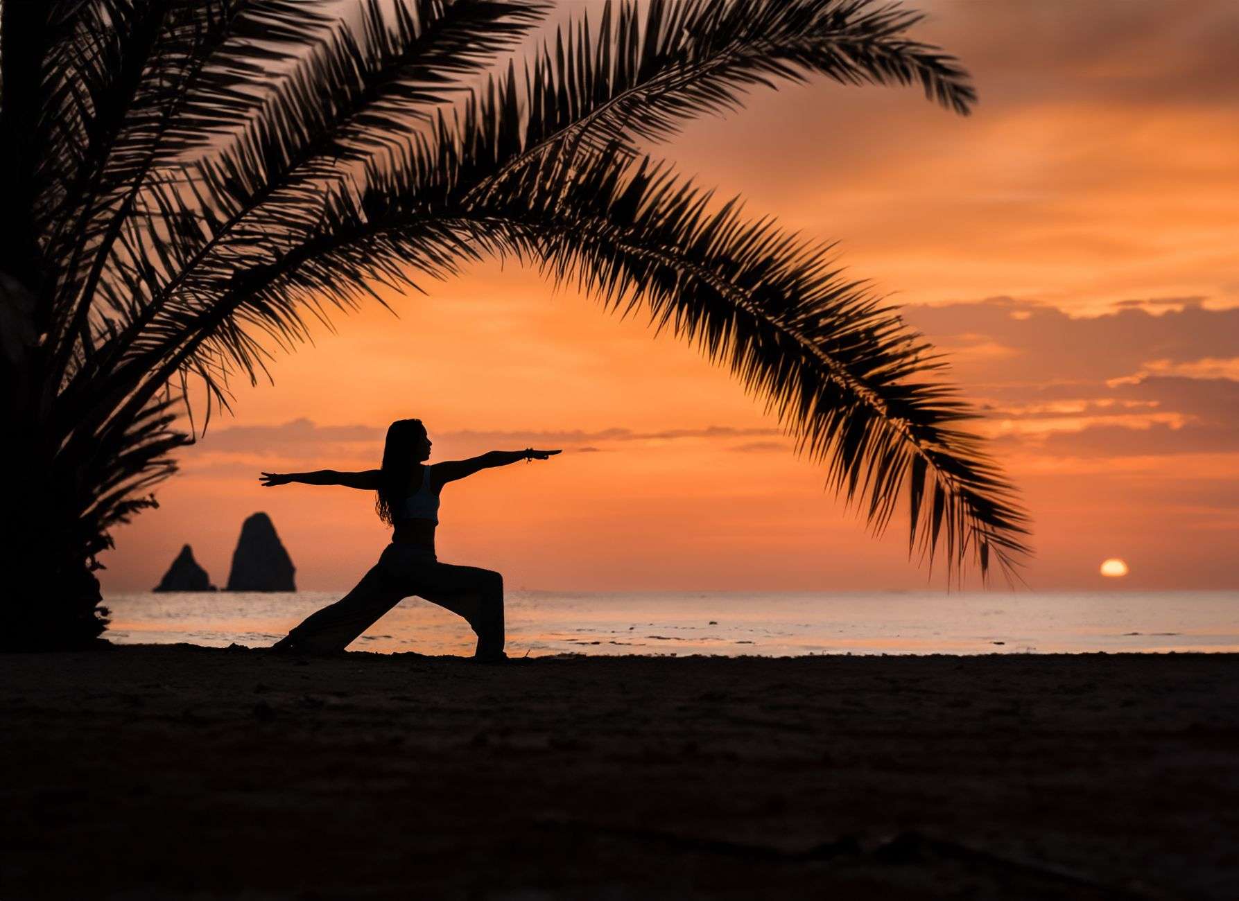 People practice yoga on a sandy beach as the sun rises over the water