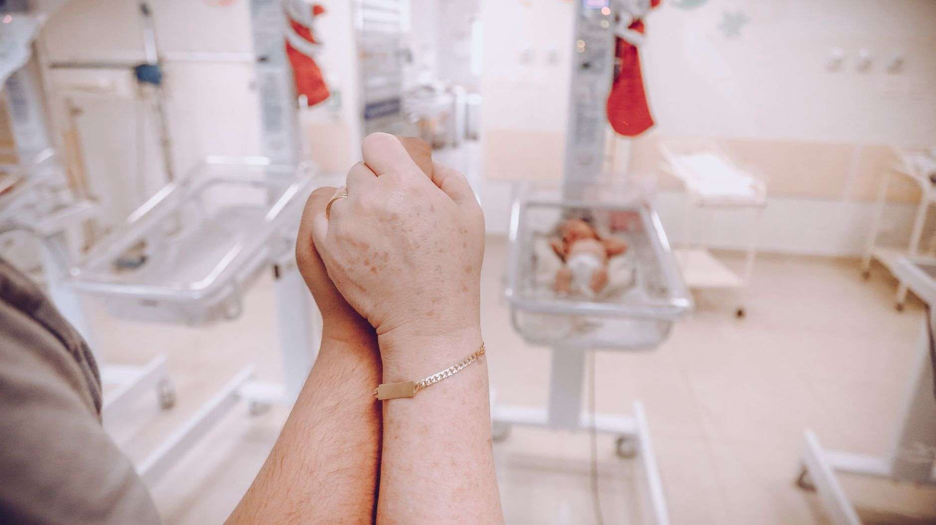 An adult's hand gently holding the tiny hand of a newborn baby