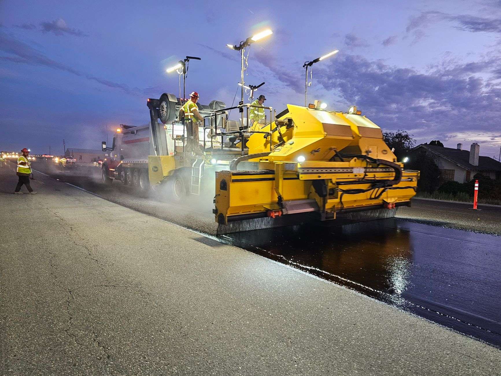 Road construction equipment resurfacing a highway at night under work lights
