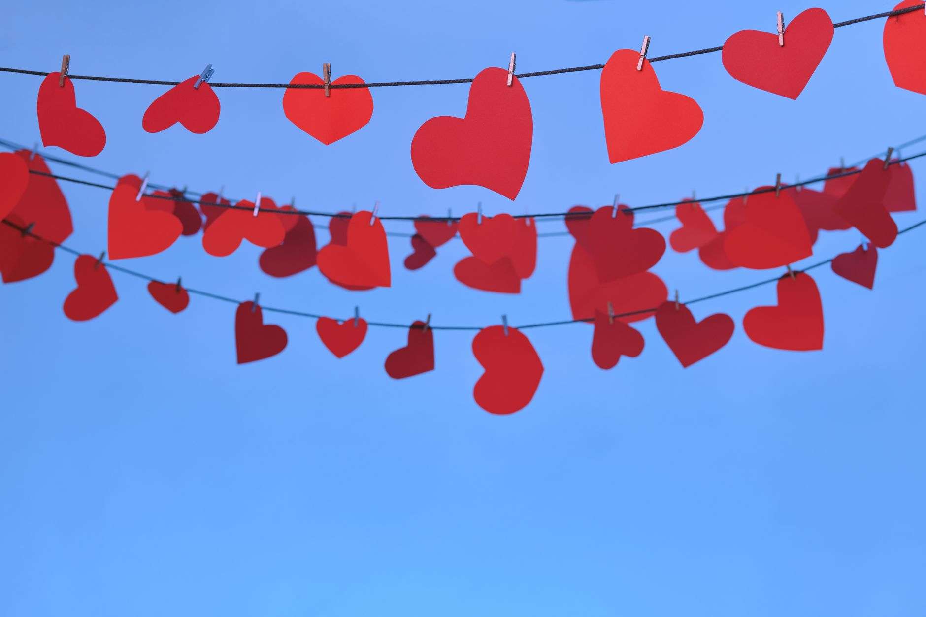 Red paper hearts hanging on strings against a blue sky