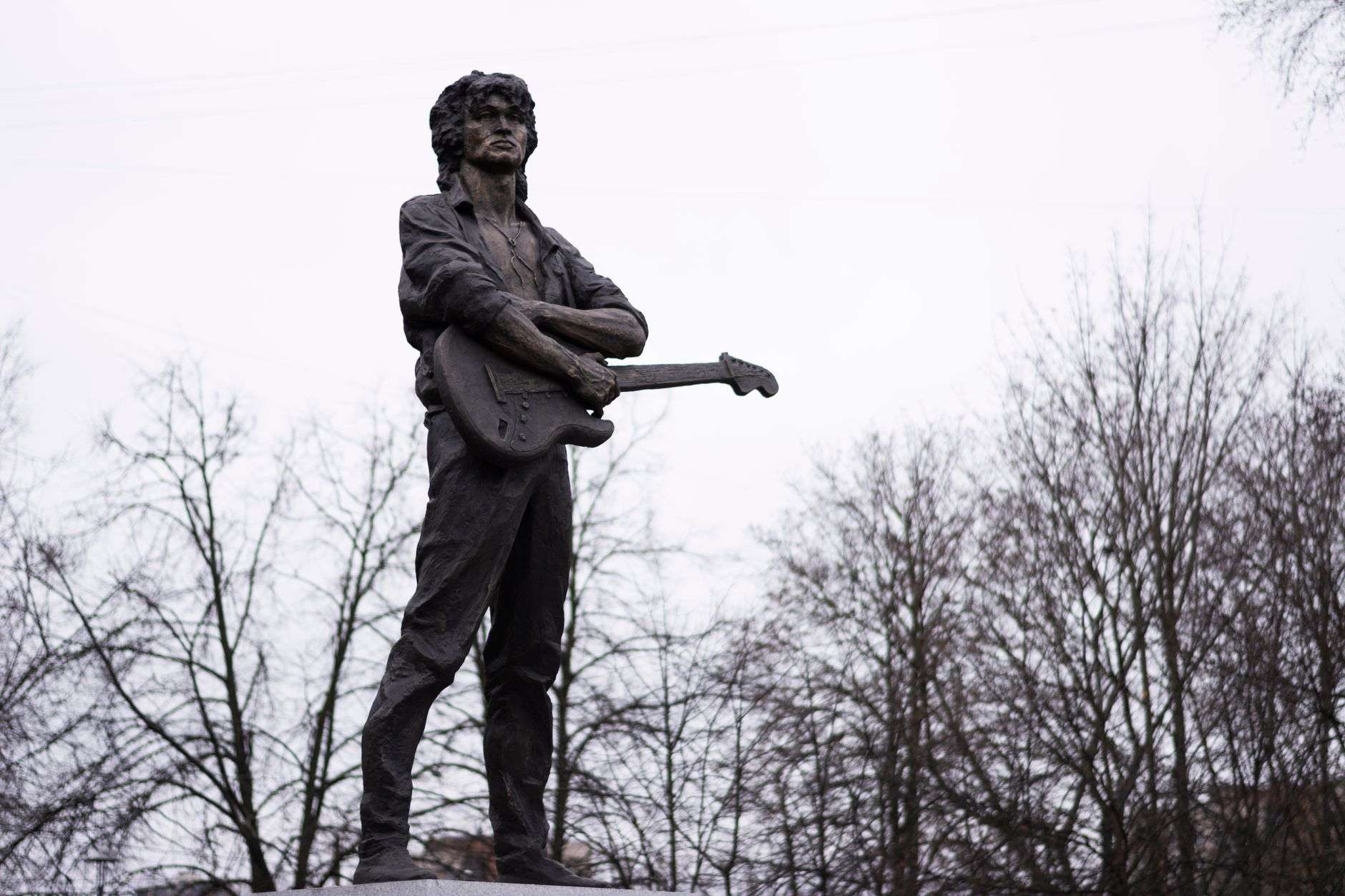 A bronze statue on a waterfront promenade facing out toward open water at daybreak