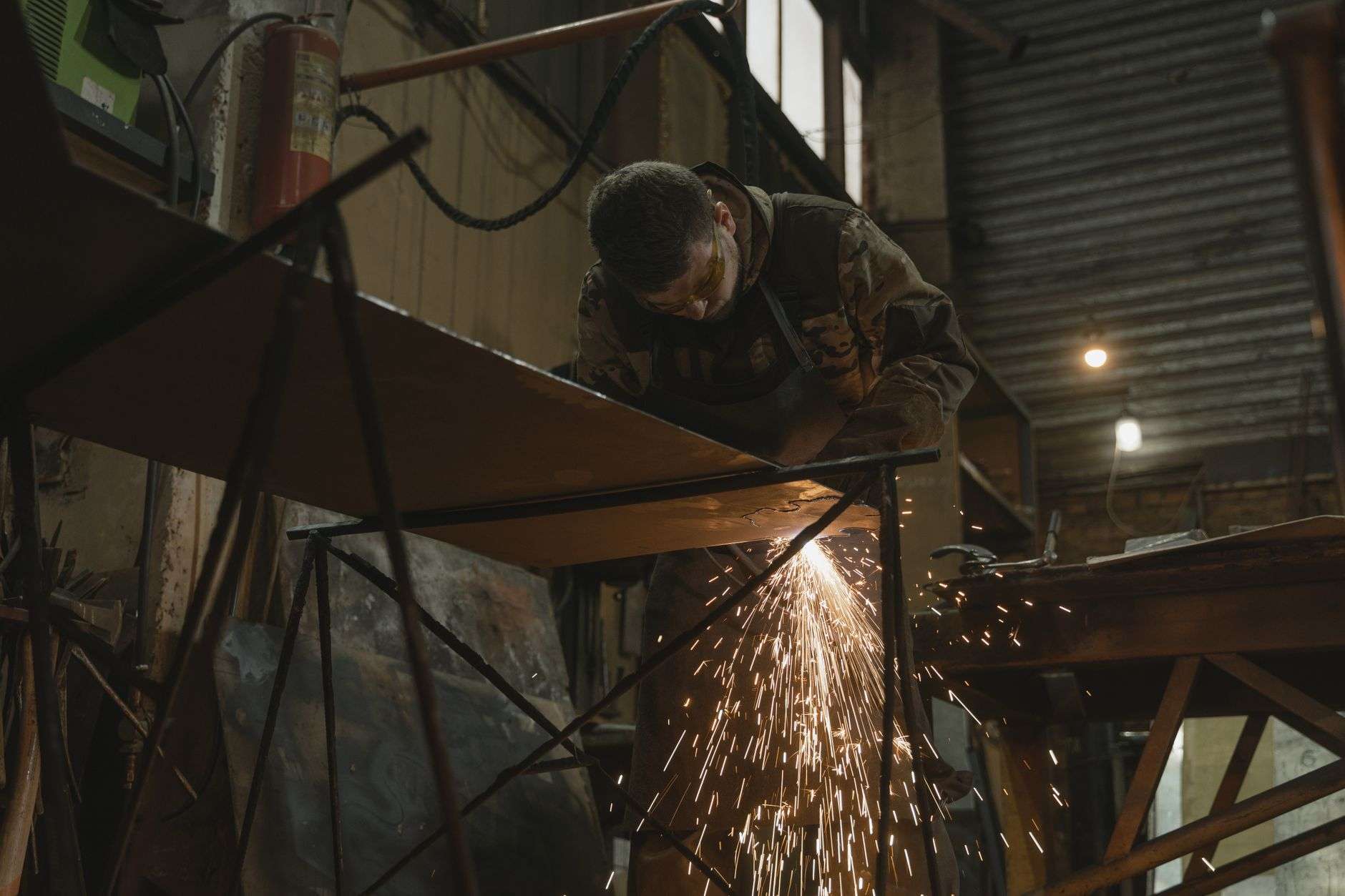 Welder working on a metal beam in an industrial fabrication shop, with sparks flying