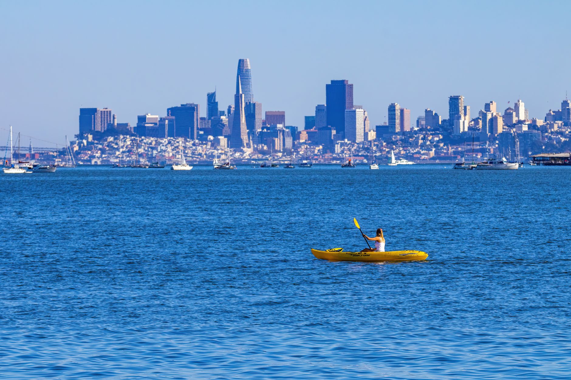 An angler casting from a fishing kayak on calm coastal water