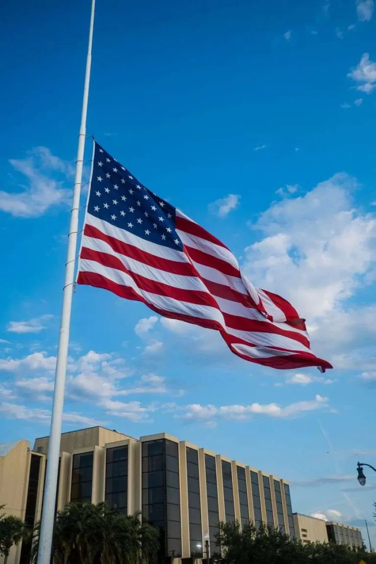 American flag flying at half-staff against a blue sky