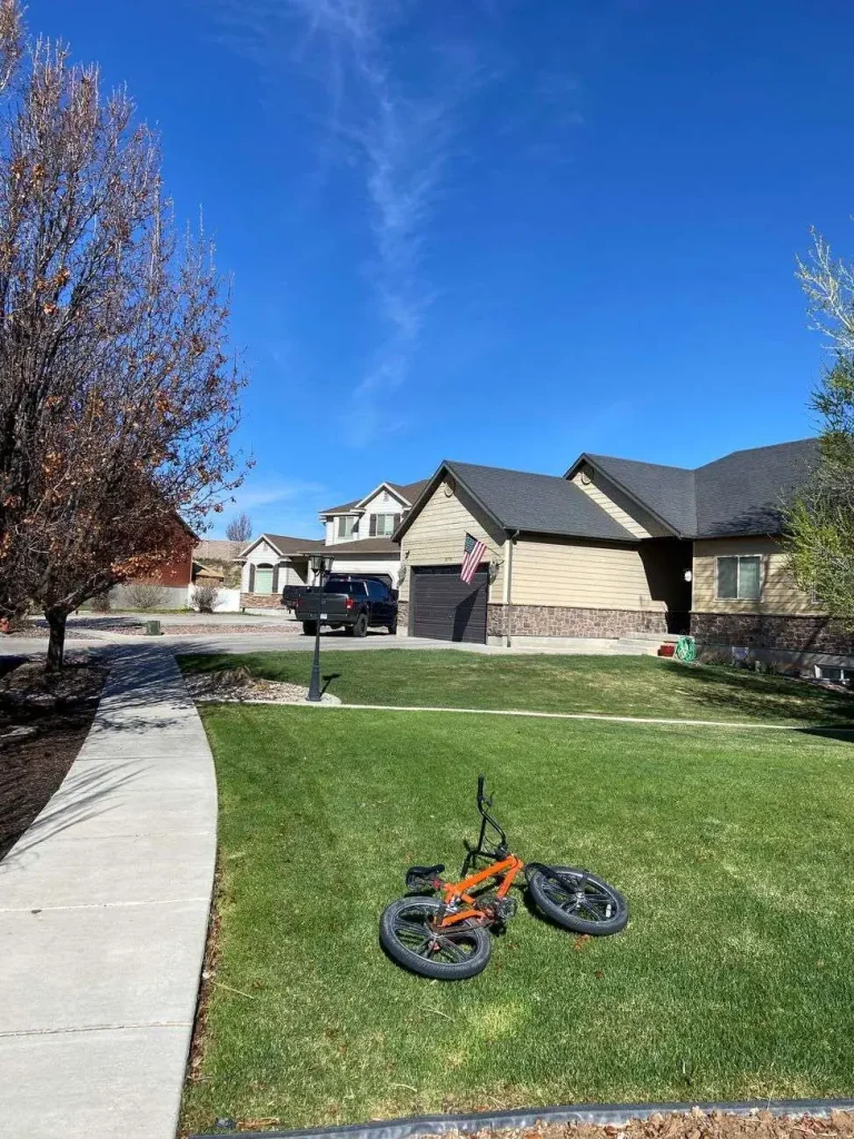A bicycle lying on the front lawn of a suburban house with a driveway and garage