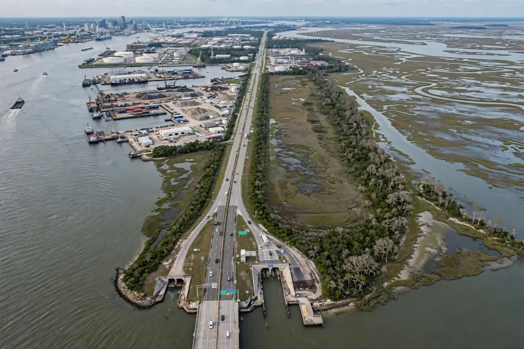 Aerial view of an industrial island with storage tanks, docks and a causeway between a river and marshland