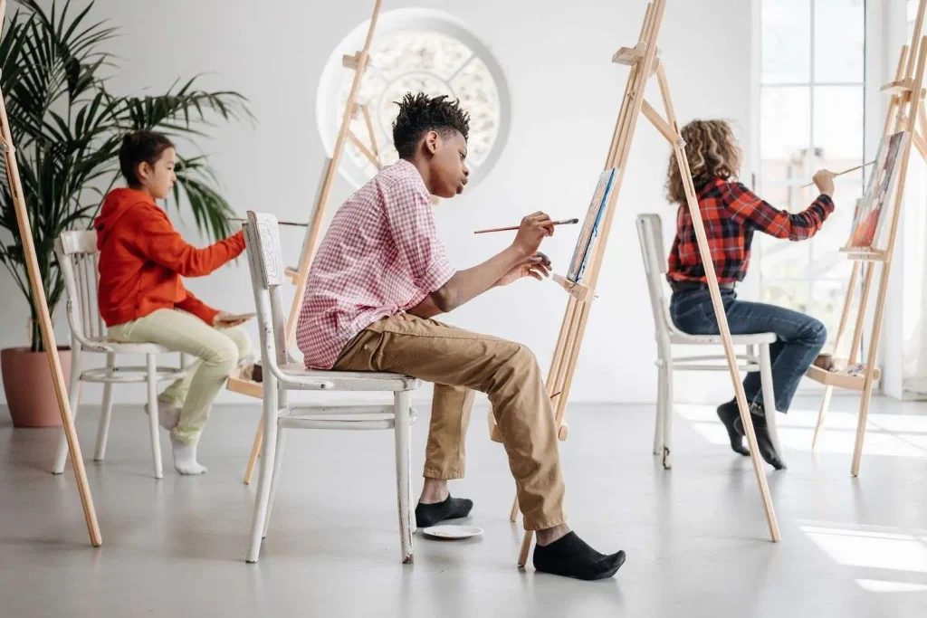 Three young people painting at easels in a bright art studio