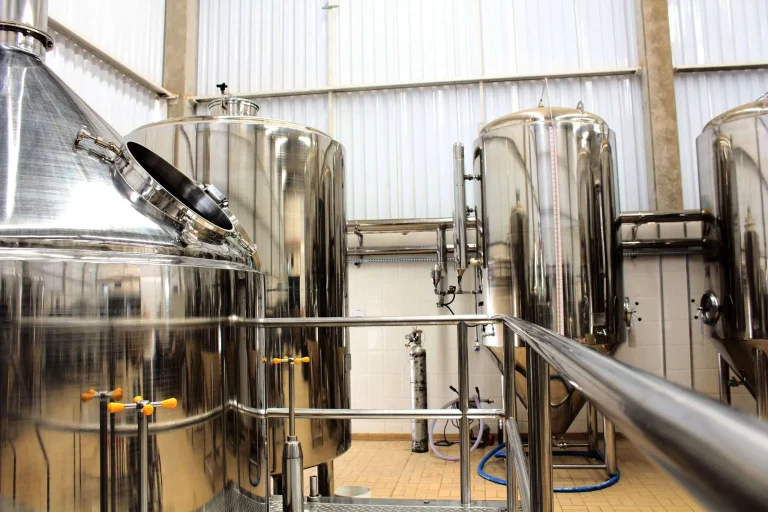 Rows of polished stainless steel brewing and fermentation tanks inside an industrial brewhouse