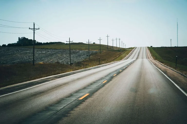Two-lane rural highway running through farmland, with utility poles and a house in the distance