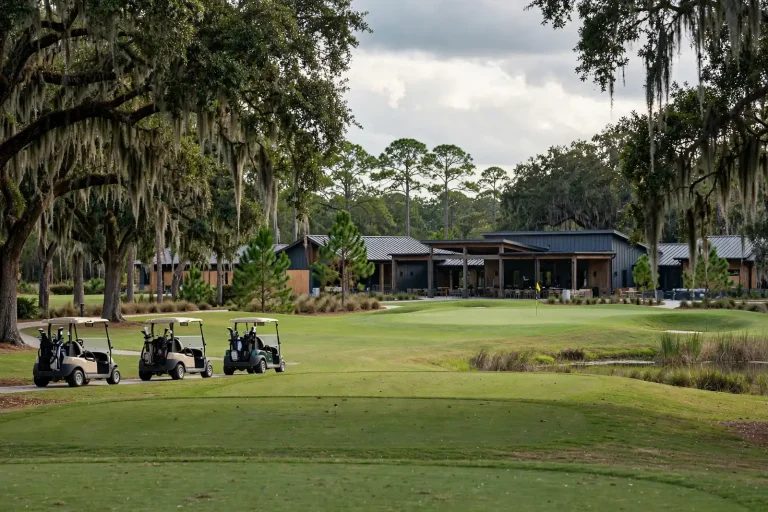 Golfers and carts on a green fairway near a clubhouse under a clear sky