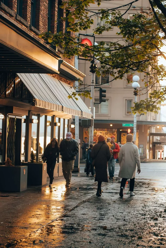 Pedestrians walking along a downtown sidewalk lined with storefronts and awnings in the evening