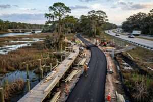 Aerial view of crews building the Eastern Shore Trail extension, with a paved path and boardwalk beside U.S. 98 near Fish River