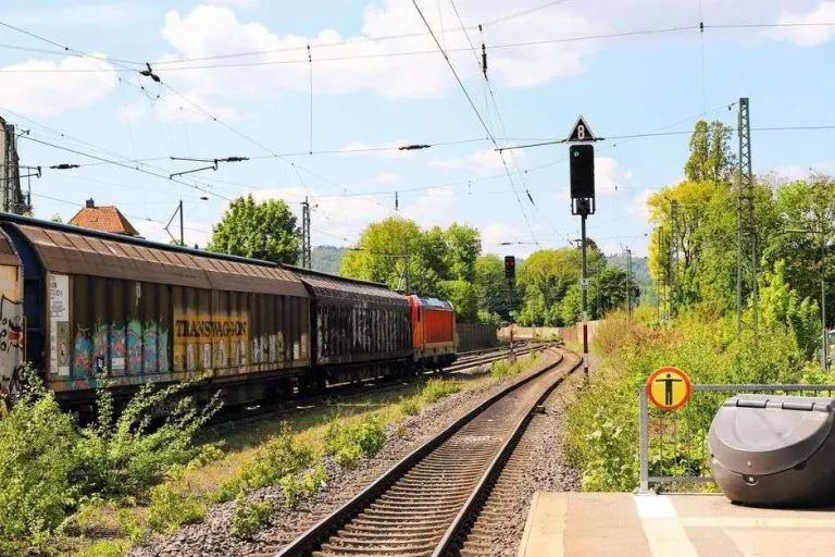 A freight train travels along railroad tracks through a green, rural landscape