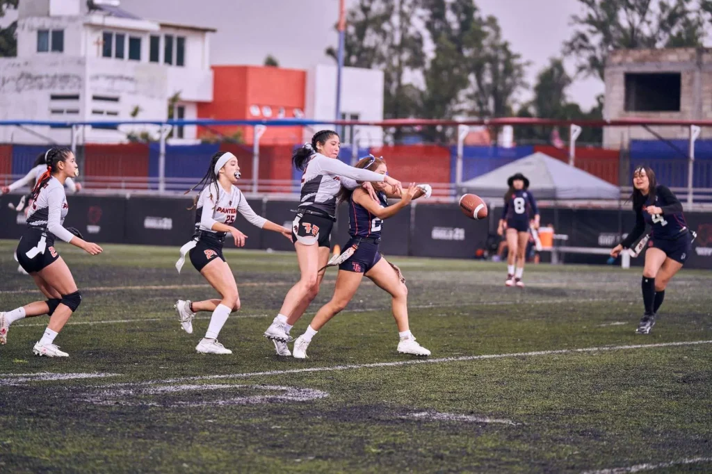 Players in a women's flag football game chasing a pass as the ball flies through the air